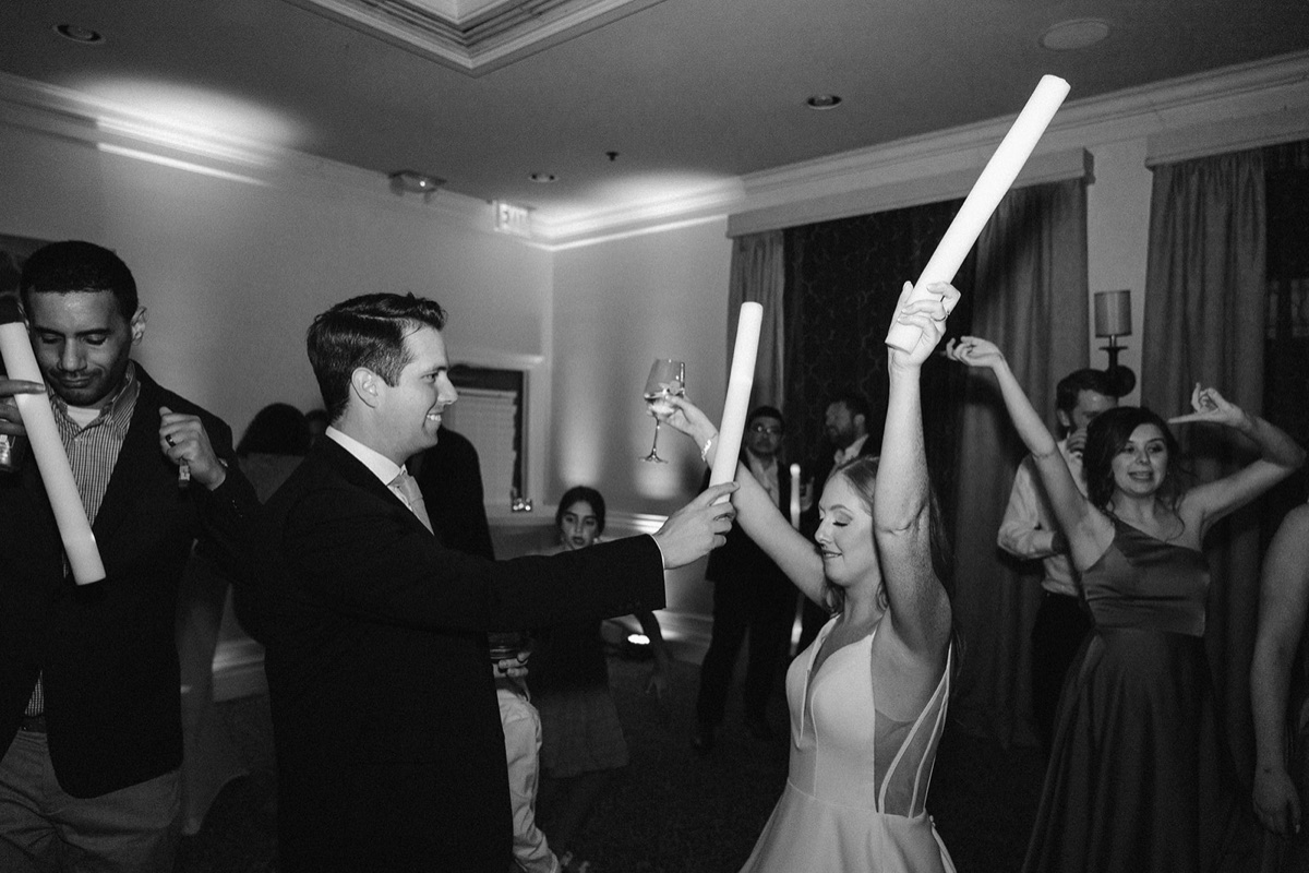 A bride and groom raising glow sticks together on the dance floor in black and white.