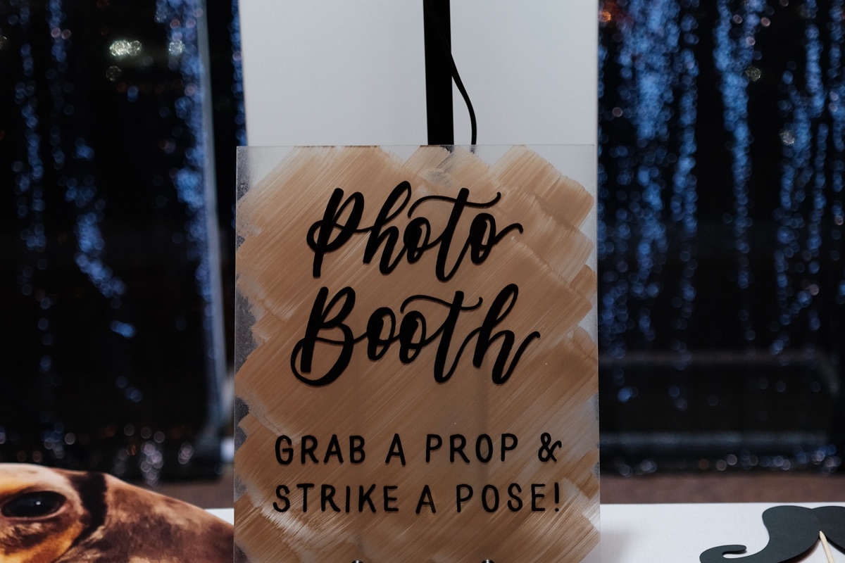 A photo booth props table under a grab a prop and strike a pose sign, cutouts and a moustache prop laid out in front of a sequin backdrop.