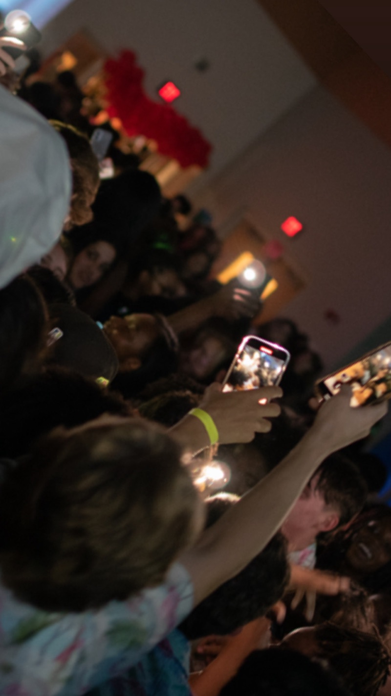 A crowd of students with phones and flashlights raised at a school dance.