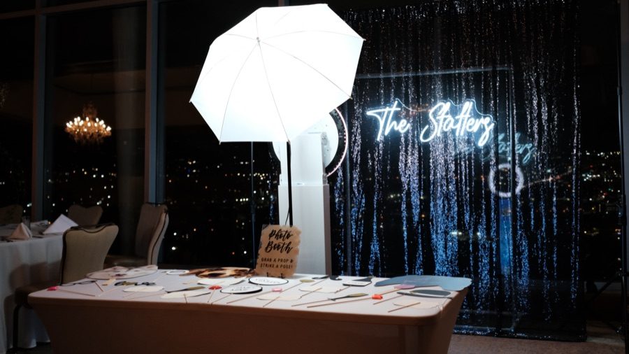 A photo booth setup with a props table and a grab-a-prop sign in front of a sequin backdrop.