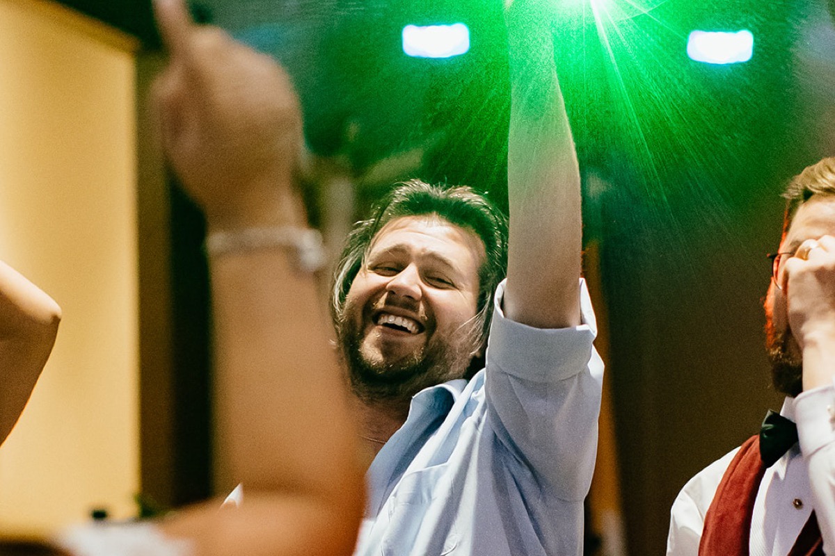 A guest cheering with one arm raised under a green stage light.